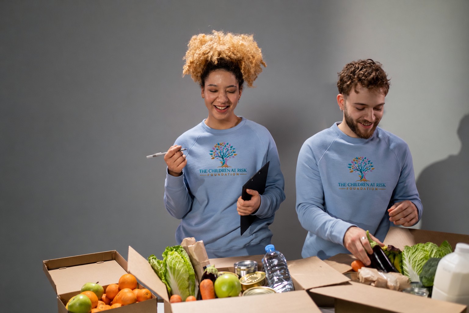 Two people wearing TCARF logo shirts packing fresh food into donation boxes